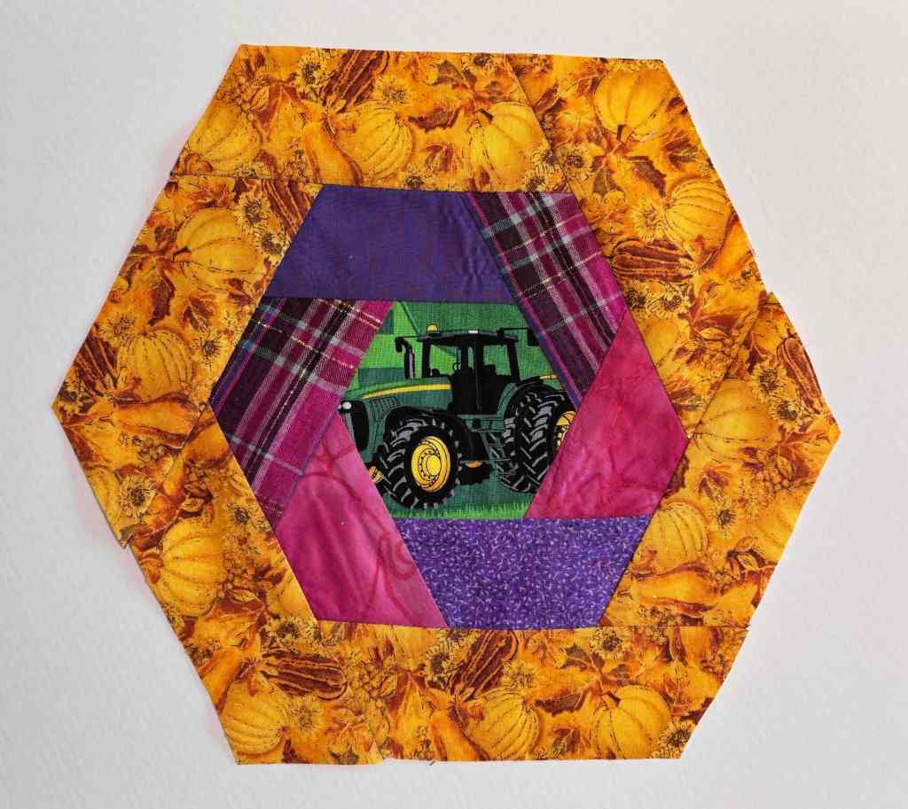 hexagon log cabin quilt block with a tractor in the center, pinks and purples in a ring around it, and yellow and orange pumpkins on the outside ring