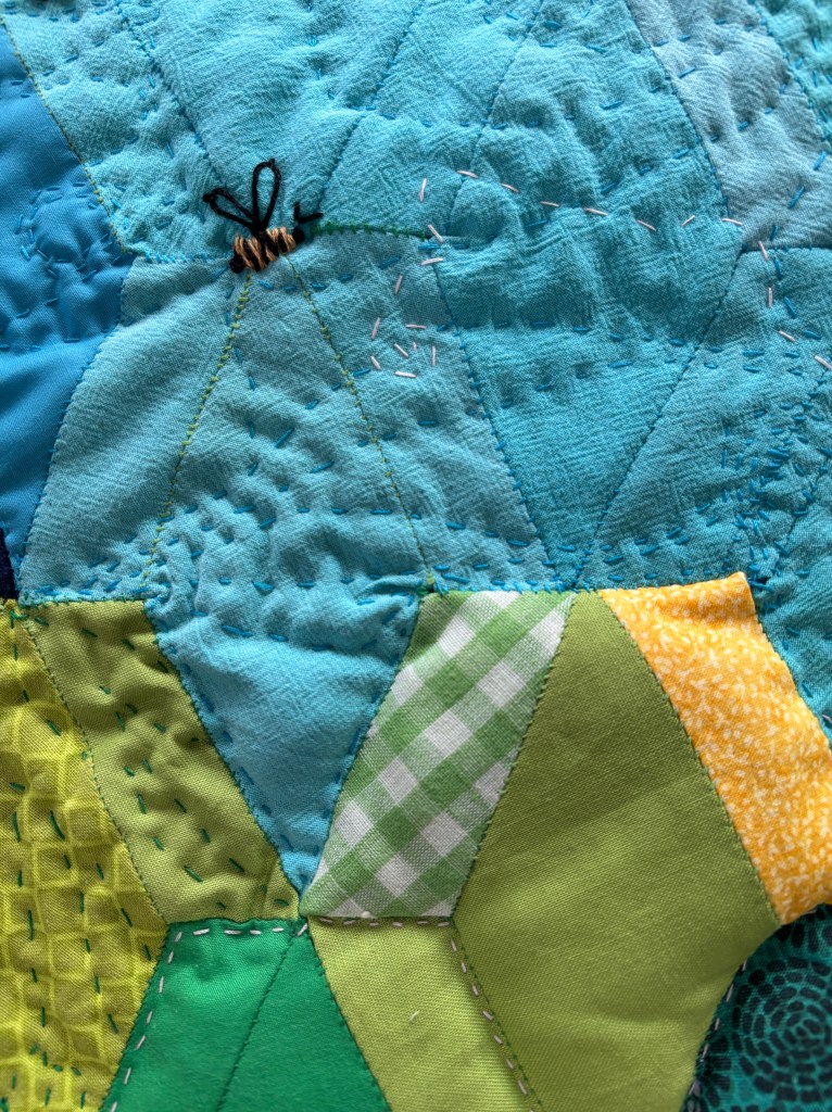 closeup of the light blue upper section of the tool holder exterior. chaotic swirling lines terminate in an embroidered bee